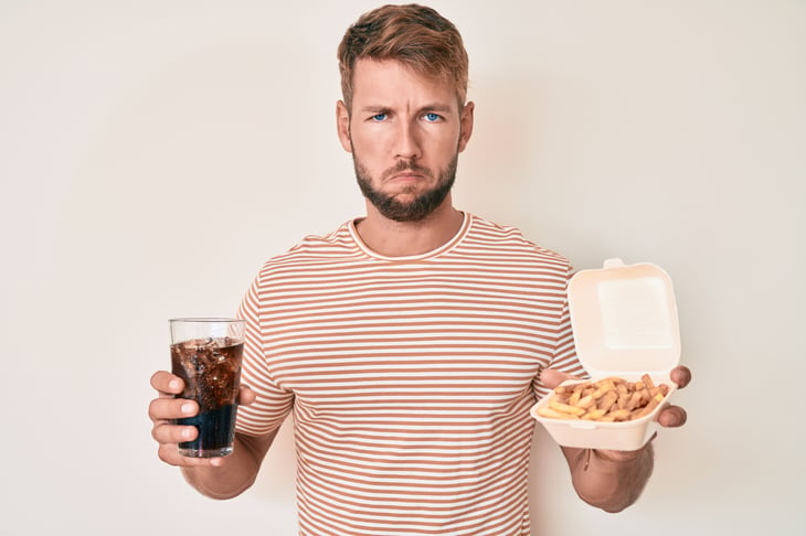 Frowning man with cola soda and fries