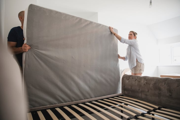 A couple places a mattress onto a bed frame