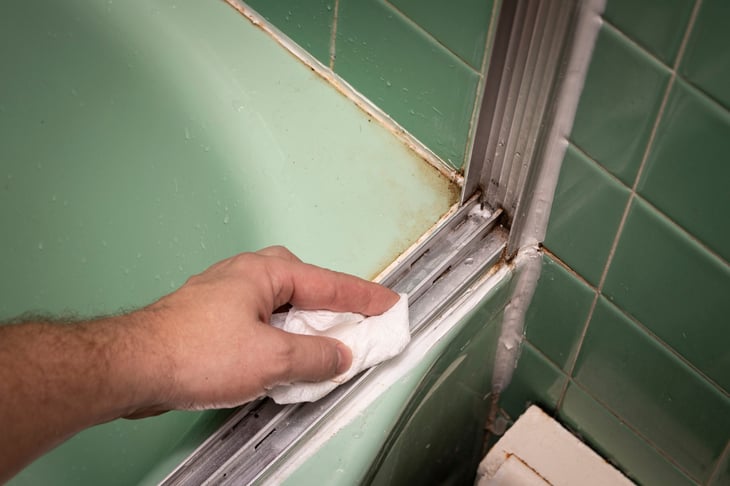 Wiping the tracks of a sliding shower door with paper towel
