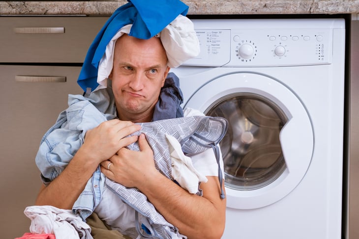 Man holding laundry confused sitting in front of washer or washing machine