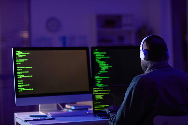 Man sitting in the dark on a computer with headphones like a spy or hacker
