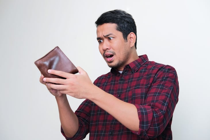 A man looking at his wallet in shock.