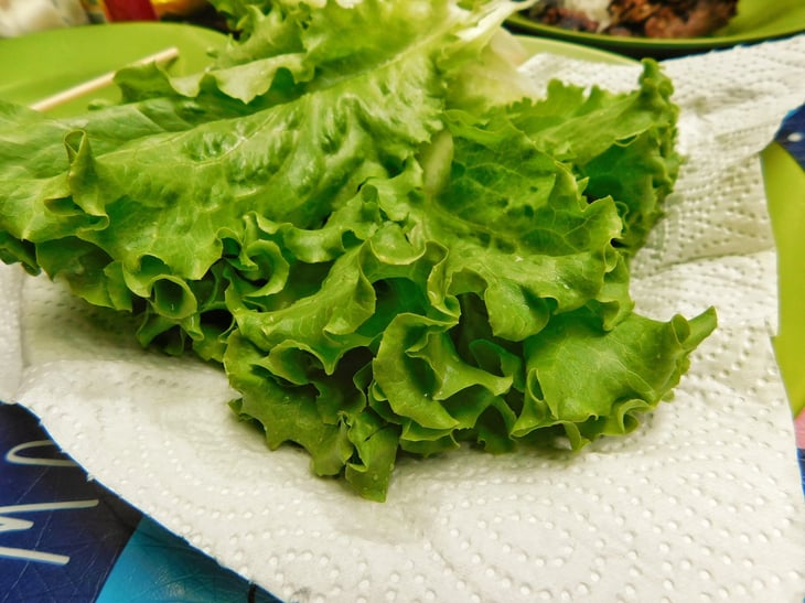 Fresh green lettuce leaves with crisp, curly edges, placed on a white paper towel.