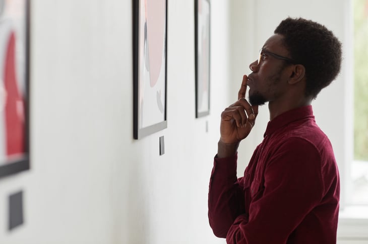 A young man looks at paintings at an art gallery
