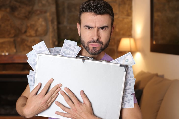 Suspicious man holding a briefcase full of money protectively, clutching his cash and angry or running with the money