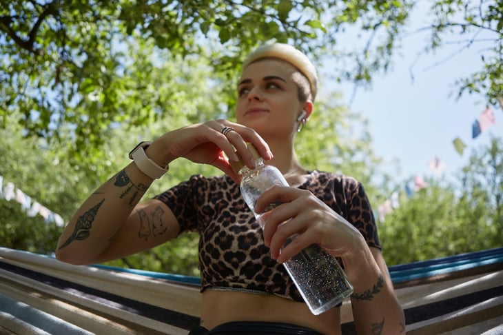 Young woman sitting on a hammock and drinking water from a reusable glass bottle