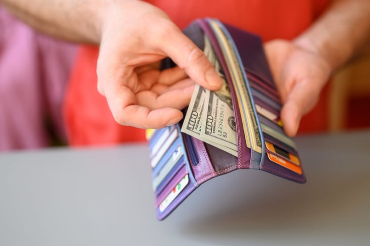 person putting cash in a wallet full of credit cards