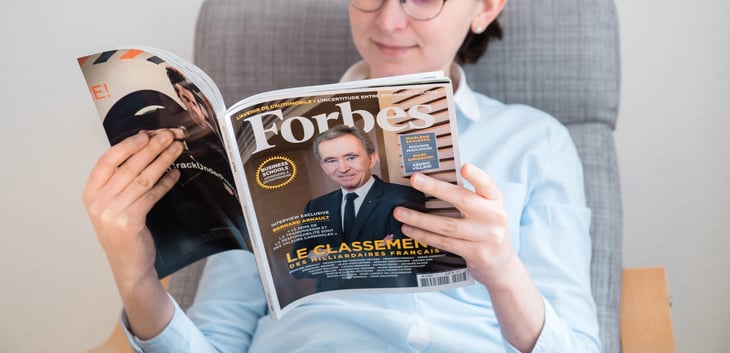 woman reading Forbes magazine with Bernard Arnault on cover