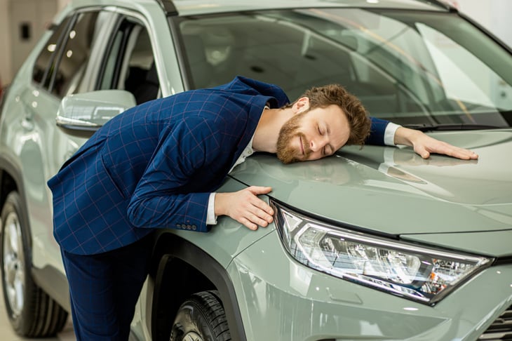 Happy man or businessman hugging a car as a new car owner or car buyer