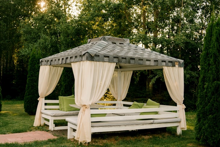 Summer gazebo terrace with outdoor sofas made of white wood, roof and curtains