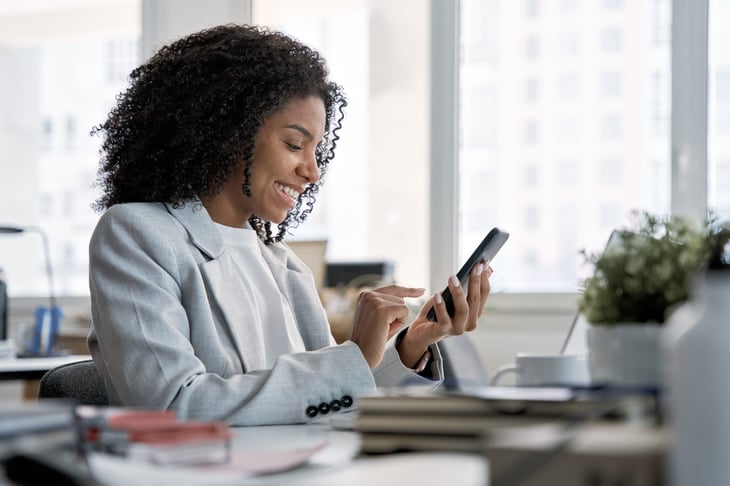 Businesswoman looking at iPhone while working at her desk in an office