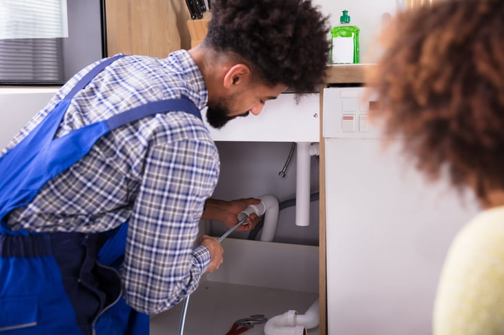 Man using drain snake to unclog kitchen sink pipe and plumbing