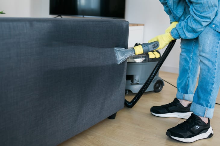 Person using a wet/dry vacuum on couch upholstery