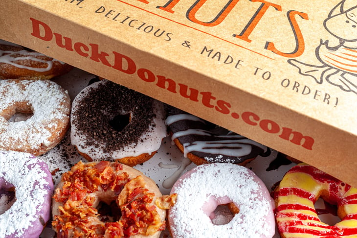 A cardboard box of a dozen donuts bought from the chain store Duck Donuts. A popular selection of assorted donuts are made to order fresh