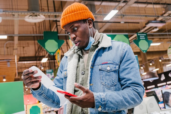 Man looking at grocery receipt and phone in surprise or excitement