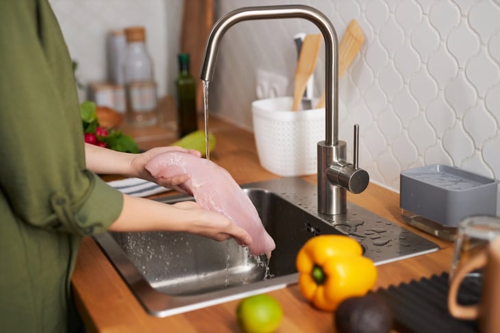 Woman washing chicken in the kitchen sink