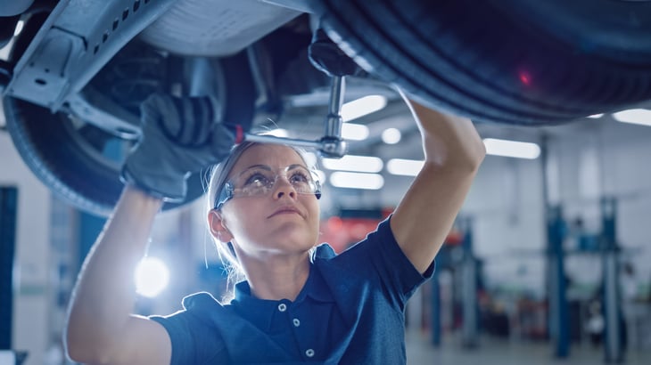 Female mechanic working on a car and doing auto repairs from below
