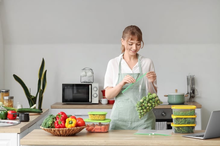 woman in kitchen putting vegetables in plastic bag