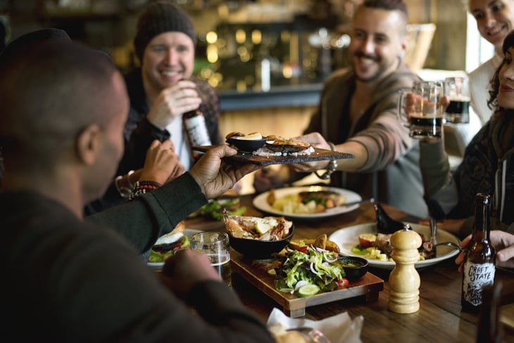 Group of friends smiling and drinking beer while eating at a restaurant