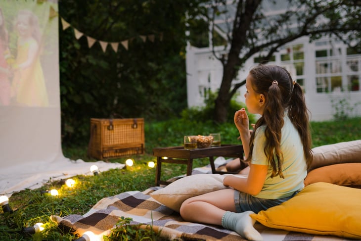 Young girl watching TV or movies on a homemade screen outdoors in the backyard at night