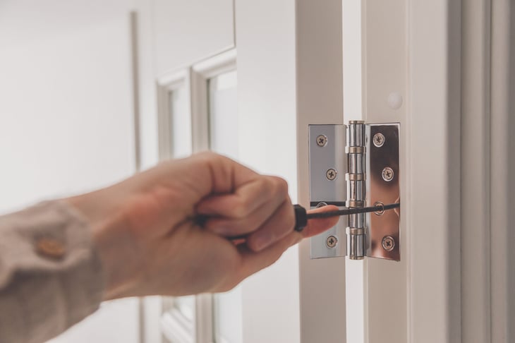 Using a screwdriver to tighten the screws on a door hinge.