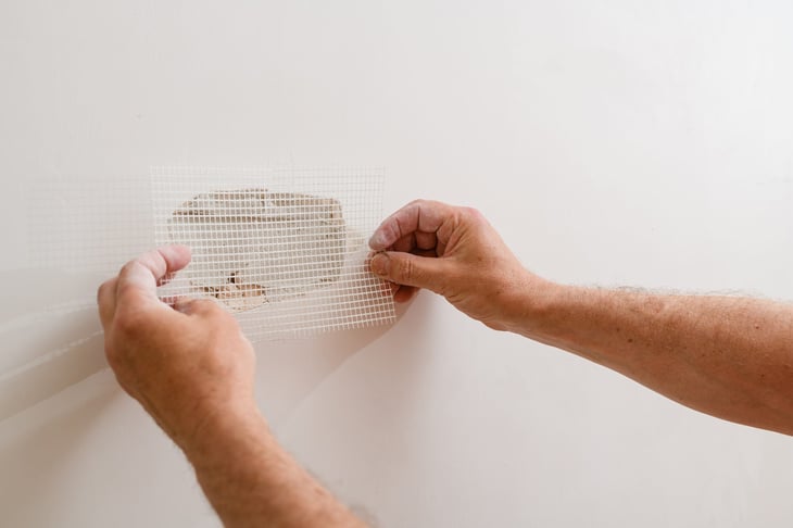 Placing mesh over a hole in drywall to repair it.