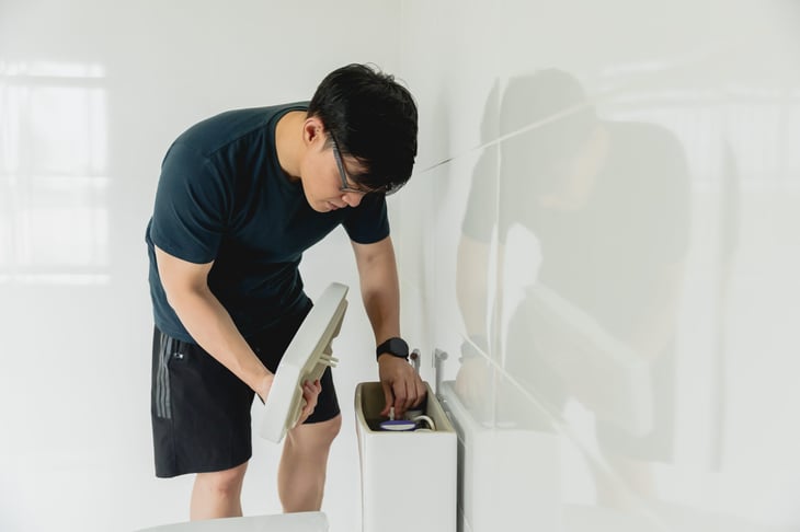 Man checking toilet tank for leaking. DIY repair.