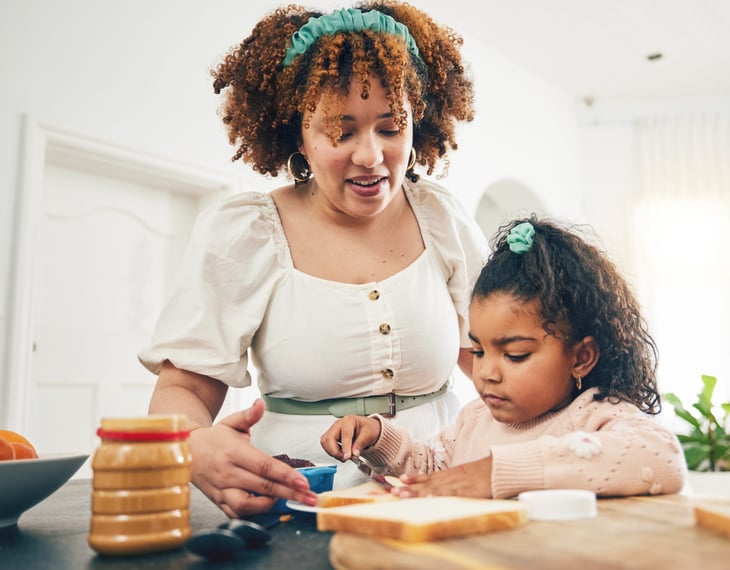 woman and kid making a peanut butter sandwich with open jar of peanut butter in the kitchen