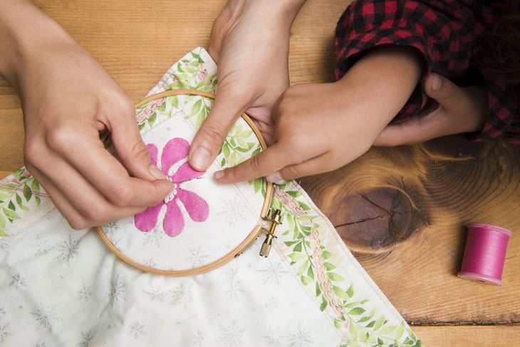 Mother and child sewing or embroidering a pillowcase with flower patterns