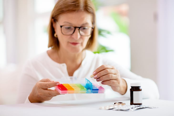 Senior woman organizing medicine with a rainbow-colored pill box or pill organizer