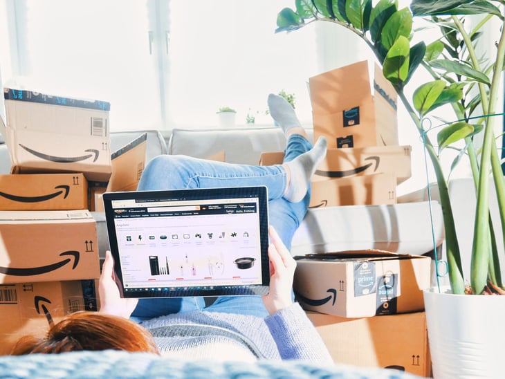Woman shopping Amazon online from laptop comfortable at home with many Amazon boxes and unopened packages