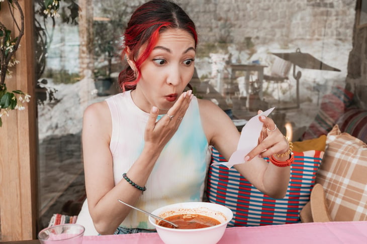 woman eating soup and surprised by restaurant bill