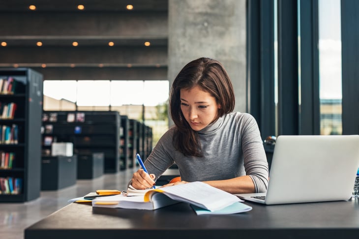 Woman studying and taking notes in the library with laptop