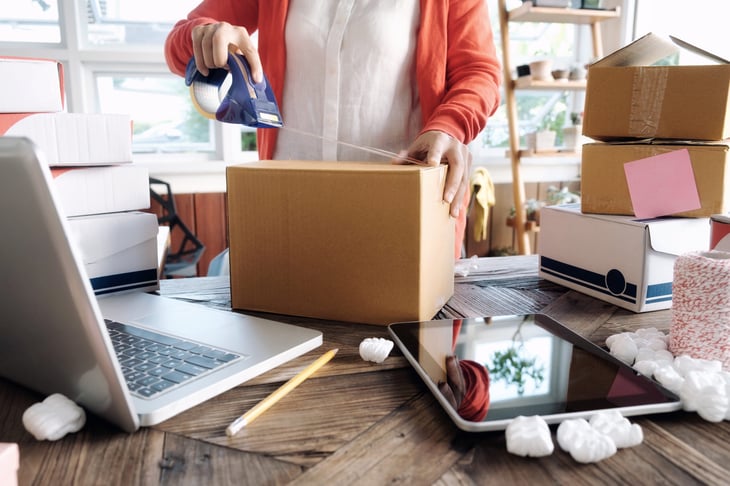Woman packing a box or wrapping a package for mailing and selling online with laptop and tablet
