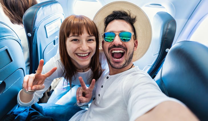 Happy excited couple in plane seats flying on vacation to have fun and showing peace sign gestures
