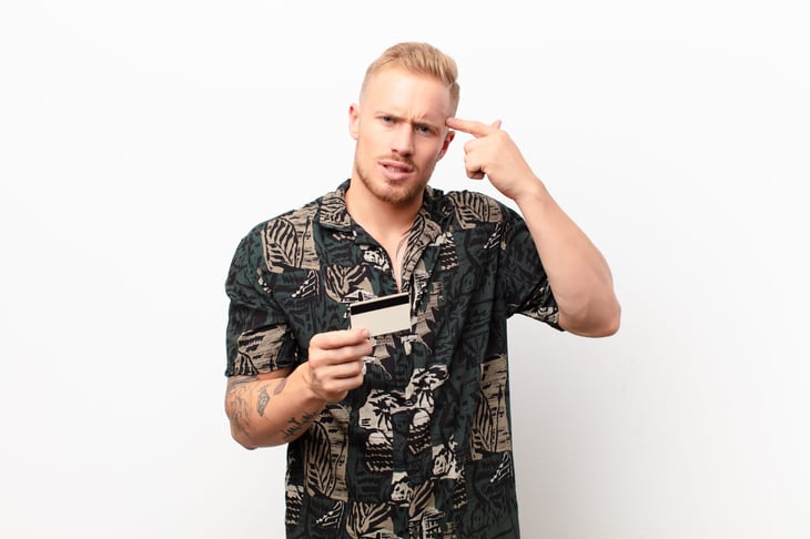 Confused man holding up a credit card and a finger to his brain