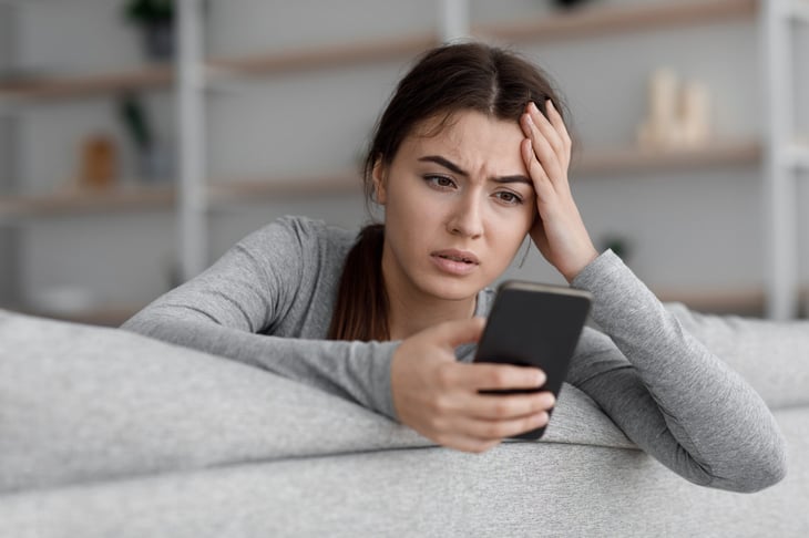 Frustrated, upset woman looking at a scam text or email on her smartphone