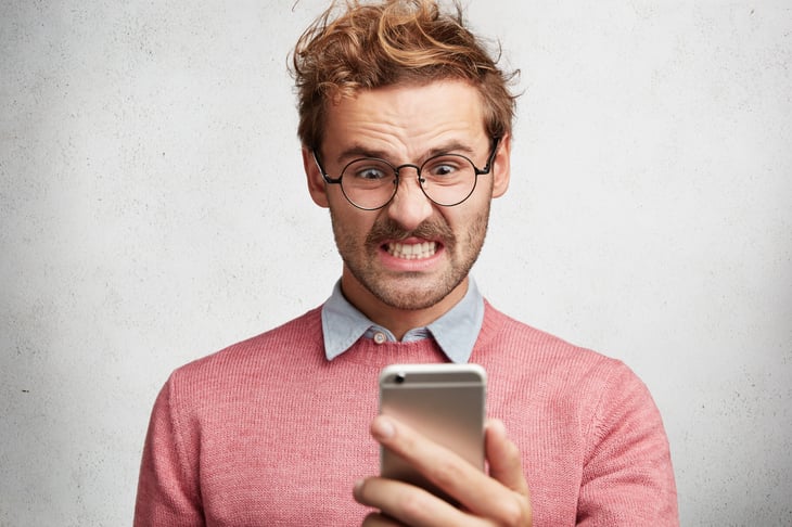 Angry frustrated man looking preppy and nerdy and upset with his cellphone bill or angry at something on his smartphone