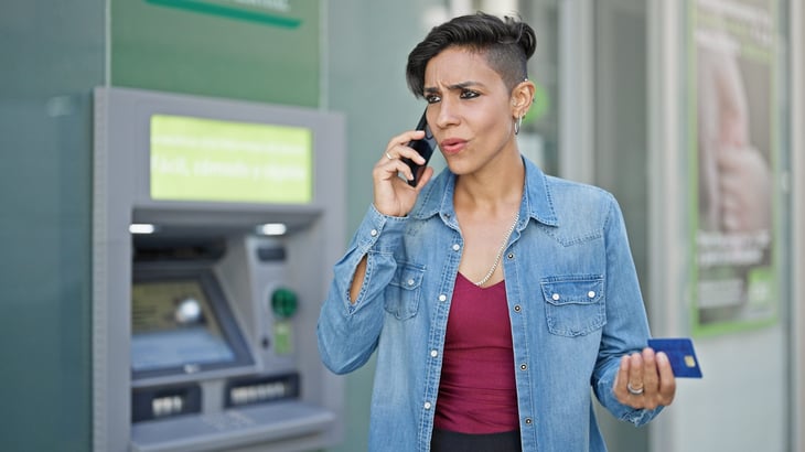 Upset woman at an ATM using a credit card or debit card for a cash advance and on the phone with bank over fees