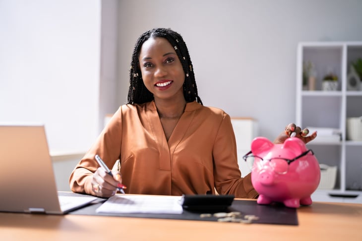 Smiling woman making a budget and planning to save money with good financial strategy represented by a smart piggy bank