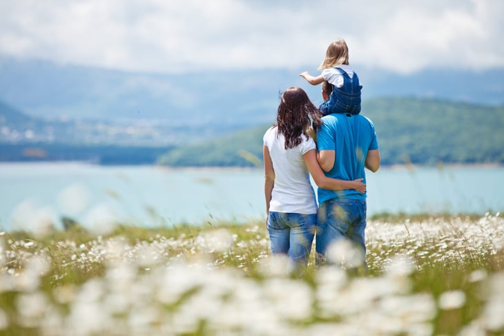 Happy family with parents and child daughter outdoors in a field of flowers overlooking the water enjoying nature