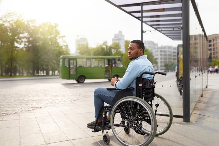 man in wheelchair waiting for public transport on bus stop
