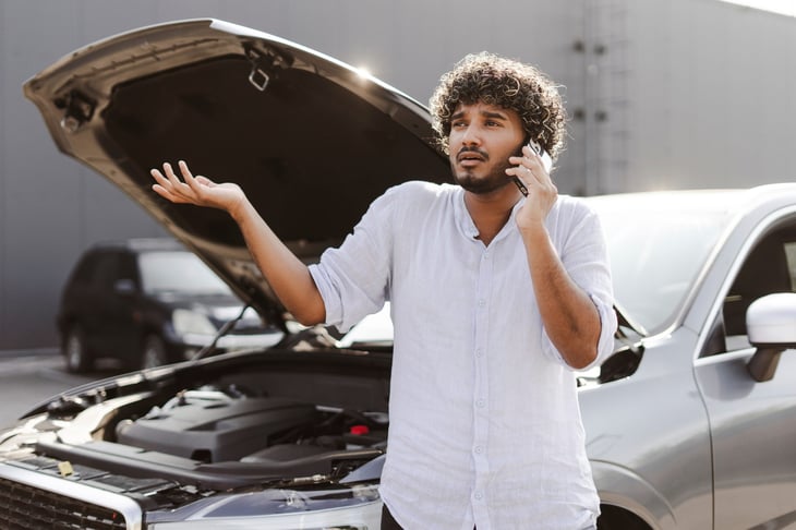 Young man with a broken down car and hood propped open on a hot summer day
