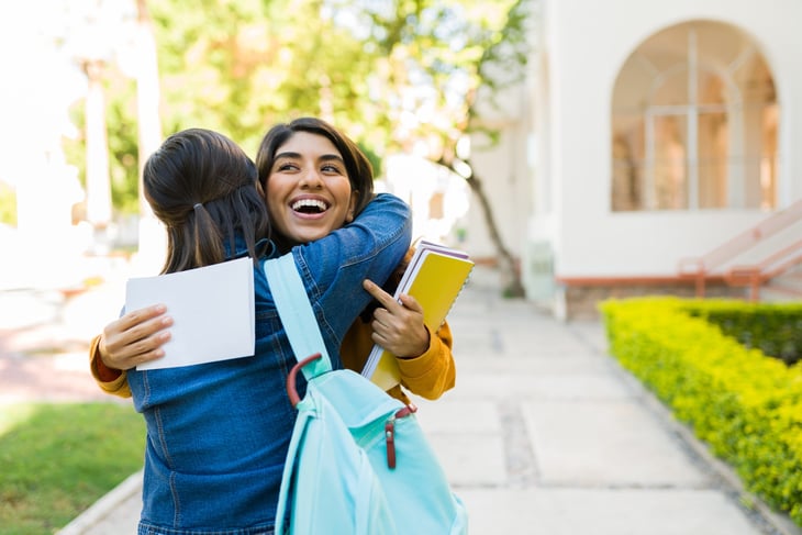 Happy high school student hugging excited friend with college acceptance letter