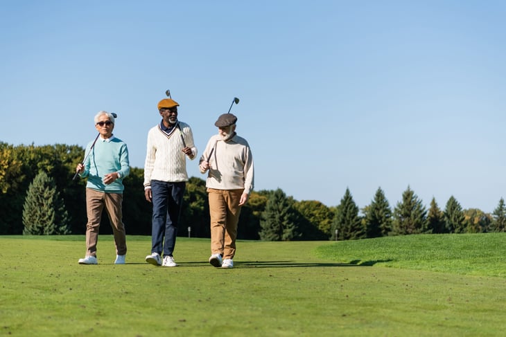 senior friends walking with golf clubs on a golf course
