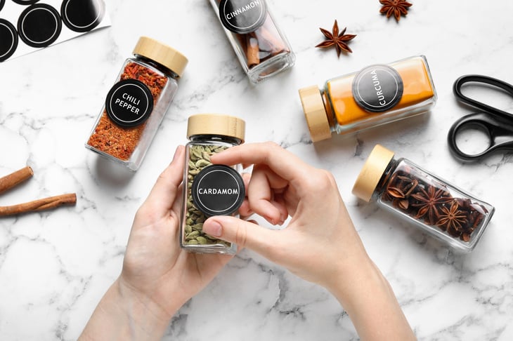 Woman labelling jar of cardamom at white marble table