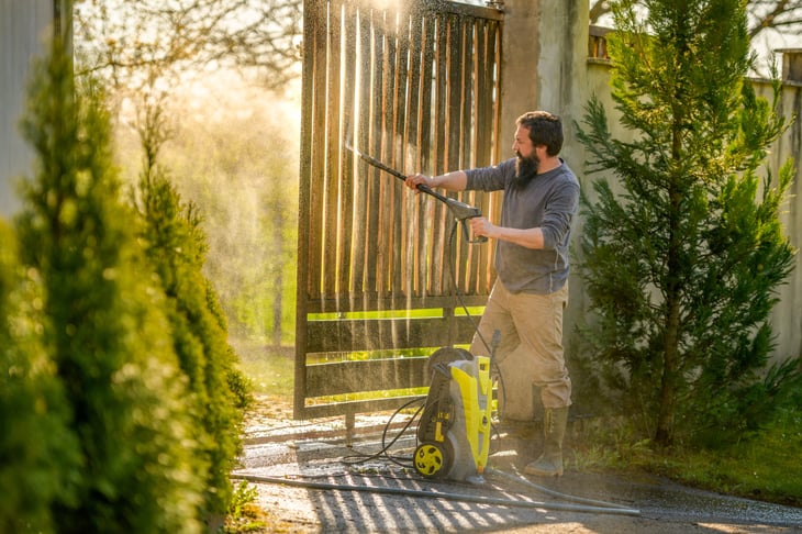 man cleaning a wooden gate with a power washer.