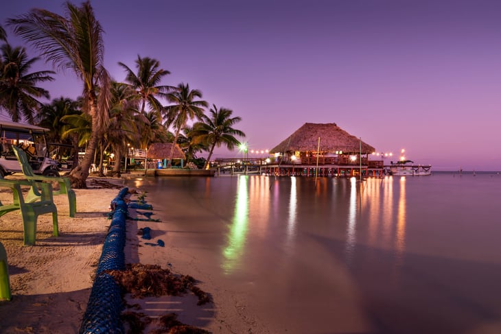 A thatched-roof bungalow over the water at sunset in Ambergris Caye, Belize.