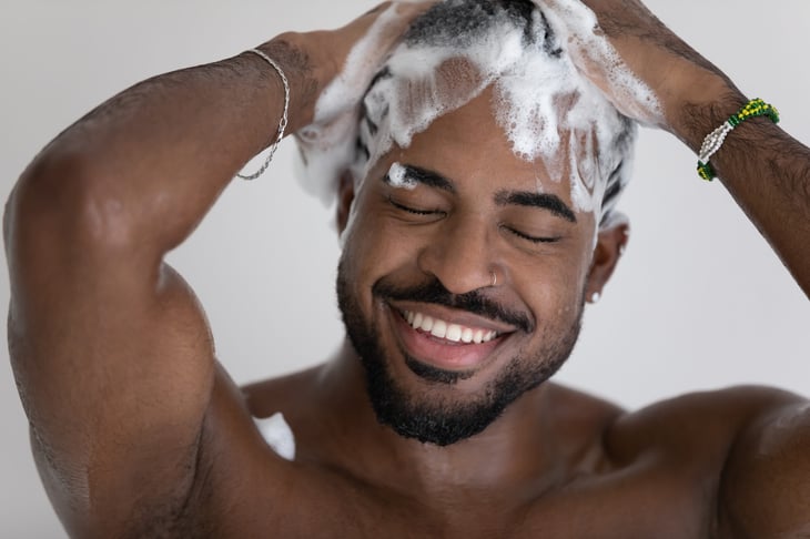 A man smiles as he shampoos his hair in the shower