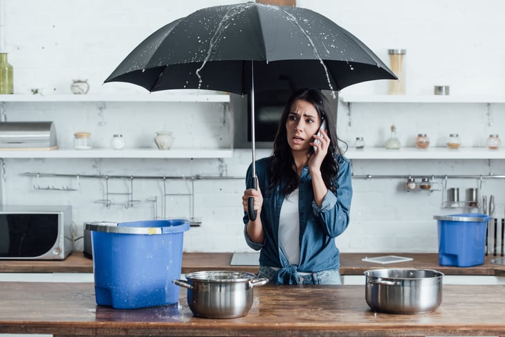 Woman with leaking roof using an umbrella in her kitchen to stay dry